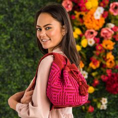 a woman carrying a pink crochet purse in front of a floral wall with flowers