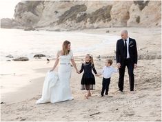 a bride and groom walking with their children on the beach in front of some cliffs