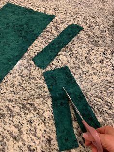 someone is cutting fabric with scissors on the counter top next to some pieces of green material