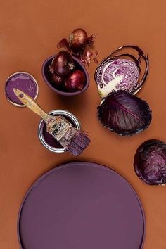 an assortment of purple vegetables on a brown table with a paint brush and bowl of onions