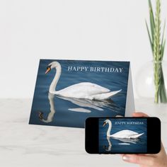 a person holding a cell phone with a happy birthday card on it next to a vase