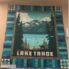 there is a quilt hanging on the wall with lake tahoe in the center and mountains in the background