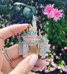 a person holding up a pin with a castle on it in front of some flowers