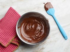 chocolate spread in a bowl next to a pink napkin and blue spatula on a white marble surface