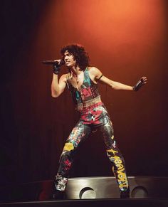 a man with long hair holding a microphone in his right hand and standing on a stage