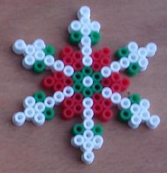 a snowflake made out of plastic beads on a wooden surface with white and green circles