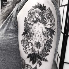 a woman's arm with a skull and flowers on the back of her shoulder