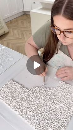 a woman in glasses is making something out of white paper on a table with scissors