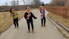 three women are walking down the road with one pointing at something in her hand while another woman is running behind them