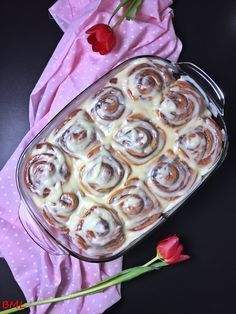 a glass dish filled with cinnamon rolls on top of a pink napkin next to a red rose