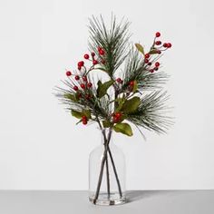 a glass vase filled with red berries and greenery