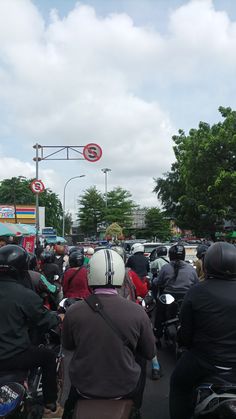 a group of people riding motorcycles down a street next to a traffic light on a cloudy day