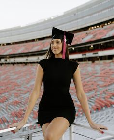 a woman in a graduation cap and gown sitting on the bleachers at a stadium