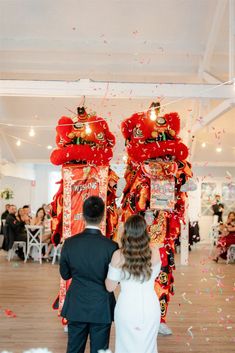 a bride and groom are standing in front of two red dragon statues as confetti falls down the floor