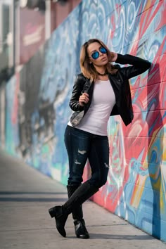 a woman leaning against a wall with her hand on her head and wearing black boots