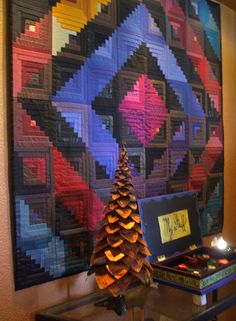 a quilt hanging on the wall next to a lit candle and a small christmas tree