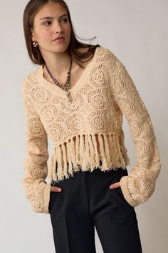 a woman is wearing a sweater with fringes on the front and back, she has her hands in her pockets