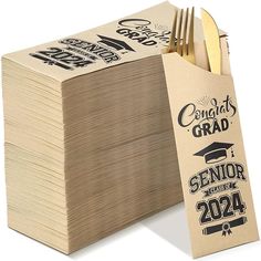 a stack of brown paper with graduation decorations on it next to a fork and knife