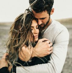 a man and woman embracing each other on the beach with long hair blowing in the wind