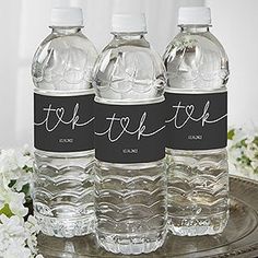 three water bottles sitting on top of a metal tray with flowers in front of them