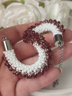 a hand holding a white and brown beaded bracelet with two silver rings on it