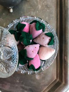 small pink and green stuffed animals in a glass bowl on top of a table next to a coin