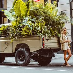 a woman standing next to a truck with plants in the back