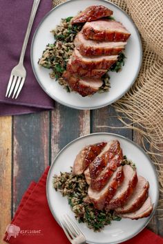 two plates filled with meat and rice on top of a wooden table next to a fork