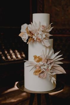 a three tiered white wedding cake with flowers on the top and bottom, sitting on a table