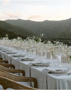 a long table is set up with white flowers and place settings for an outdoor dinner