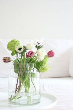 a glass vase filled with flowers on top of a white table next to a couch