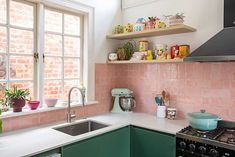 a kitchen with green cabinets and pink tile backsplash, white counter tops and shelves