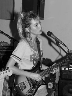 a woman playing guitar while standing in front of a microphone and sound equipment behind her