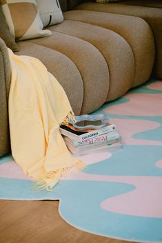 a pile of books sitting on top of a blue and pink rug next to a couch