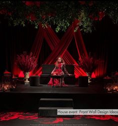 a woman sitting on top of a black couch in front of a red stage curtain