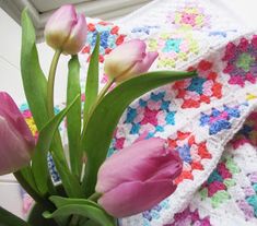 pink tulips are in a vase on a table next to a crocheted blanket