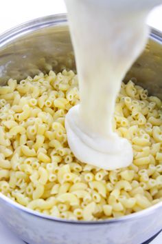 a person pouring milk over macaroni and cheese in a pot