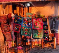 several colorfully embroidered items are displayed on the outside of a hut with wooden poles