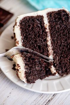 a slice of chocolate cake with white frosting on a plate and a fork next to it