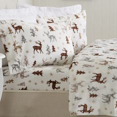 a bed with white sheets and brown deers on it, next to a night stand