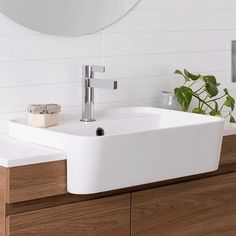 a white sink sitting on top of a wooden counter next to a mirror and potted plant