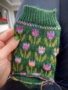 a person holding up a green knitted item with pink and yellow flowers on it