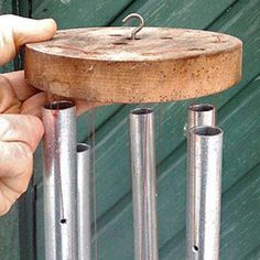 a person is holding an old wind chime in front of a green door with metal tubes