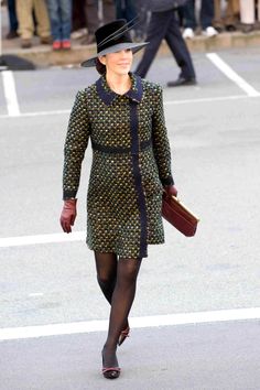 a woman in a dress and hat walks down the street while people watch from behind her