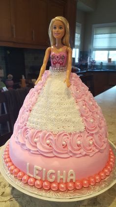 a barbie doll cake with pink and white frosting on it's top, sitting on a table