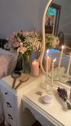 a white dresser topped with a mirror and candles next to a vase filled with flowers