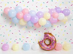 a donut with sprinkles sitting in front of balloons and confetti