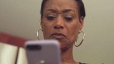 a woman looking at her cell phone while she is in front of the mirror with an upset look on her face