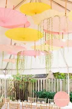 many umbrellas are hanging from the ceiling above chairs and tables in an outdoor venue