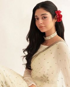 a woman with long black hair wearing a white sari and red flower in her hair